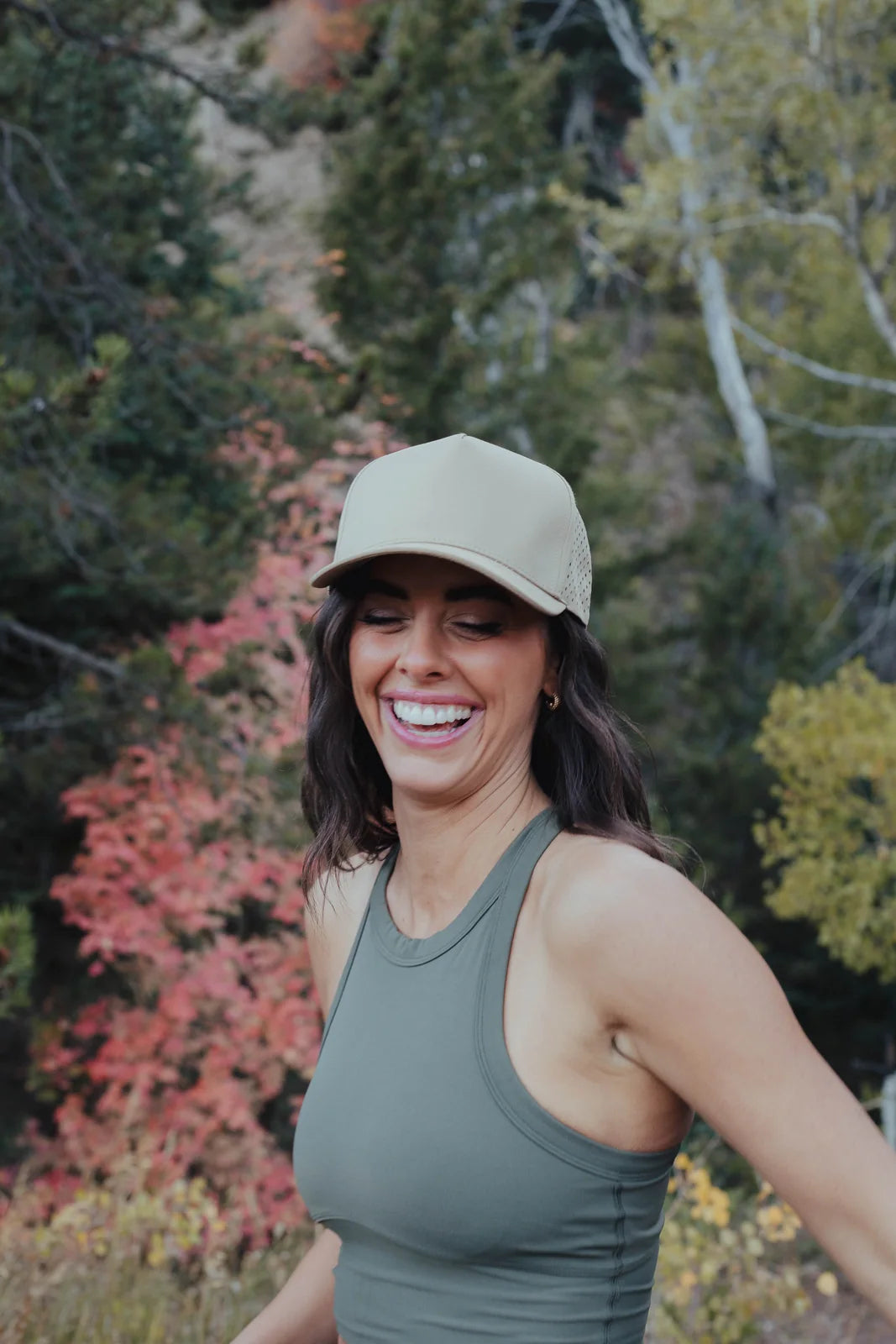 Smiling woman wearing a green sleeveless athletic top and cap outdoors